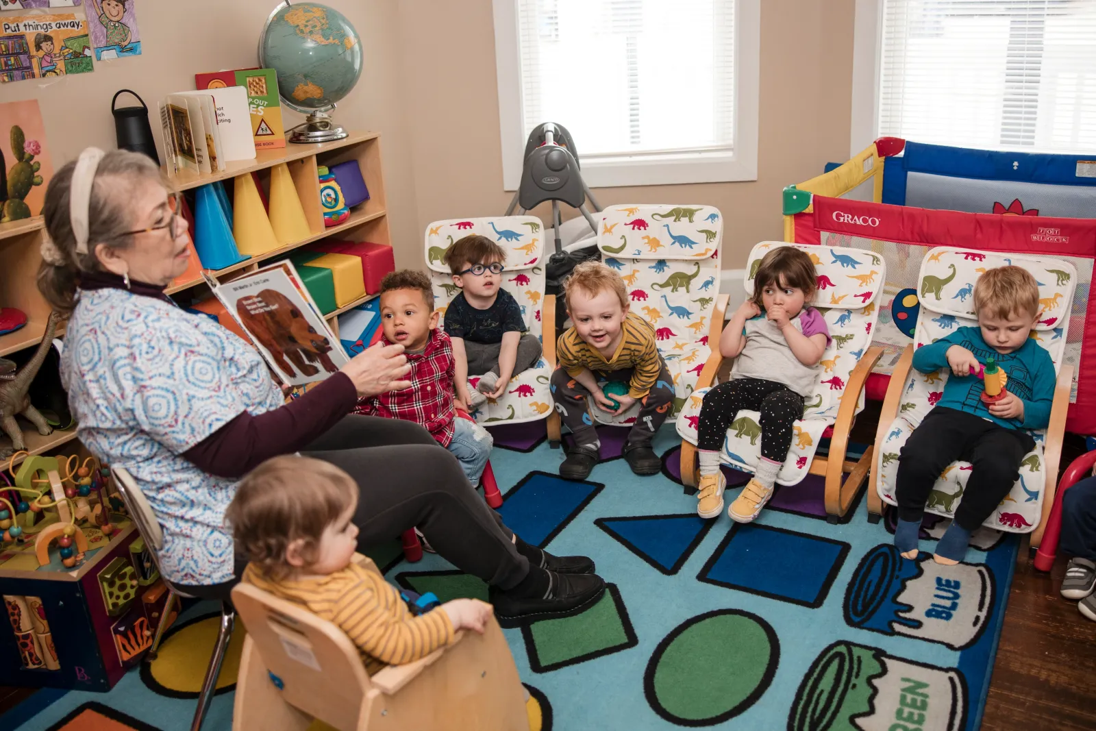 Children settled into a row of cozy chairs on the rug while a caregiver reads aloud.