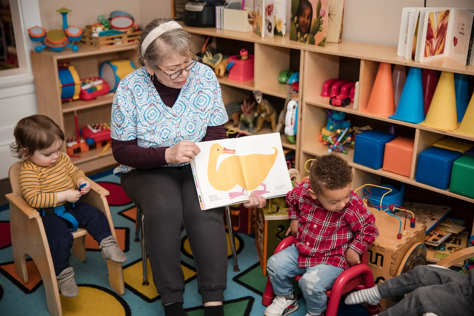 Storytime: a caregiver holds up a picture book for children in the reading corner.