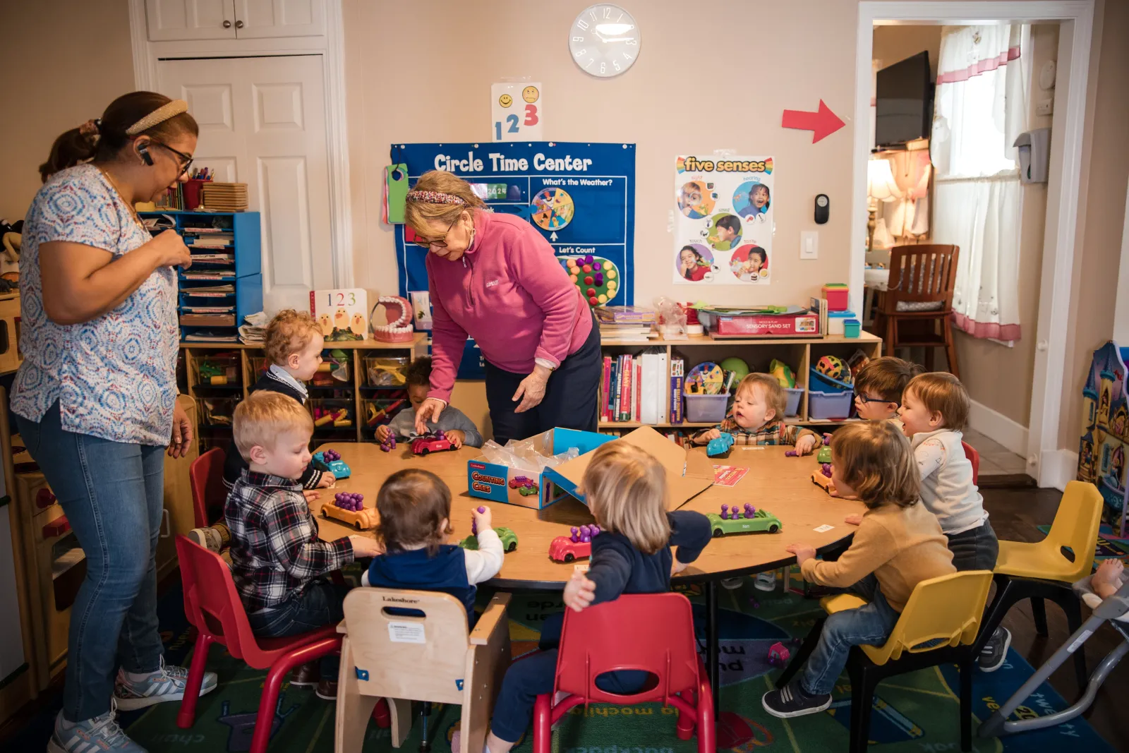 Circle time — two caregivers and a group of children gathered at the table.