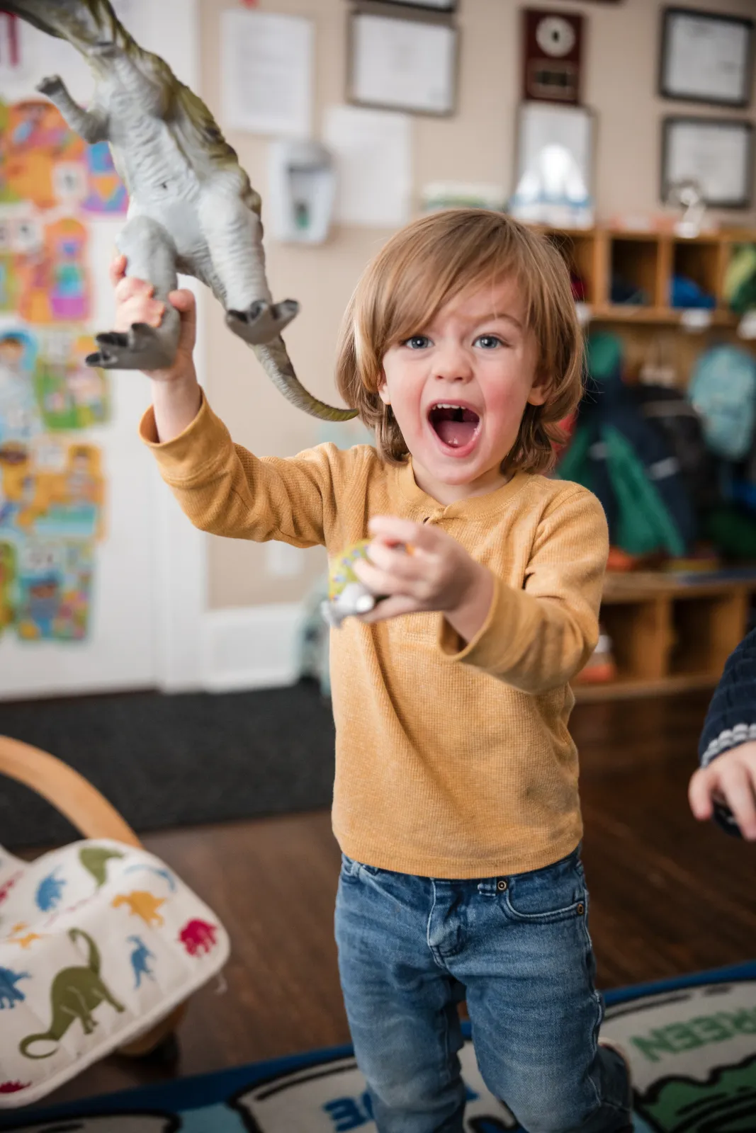 An excited toddler holding up a toy dinosaur.