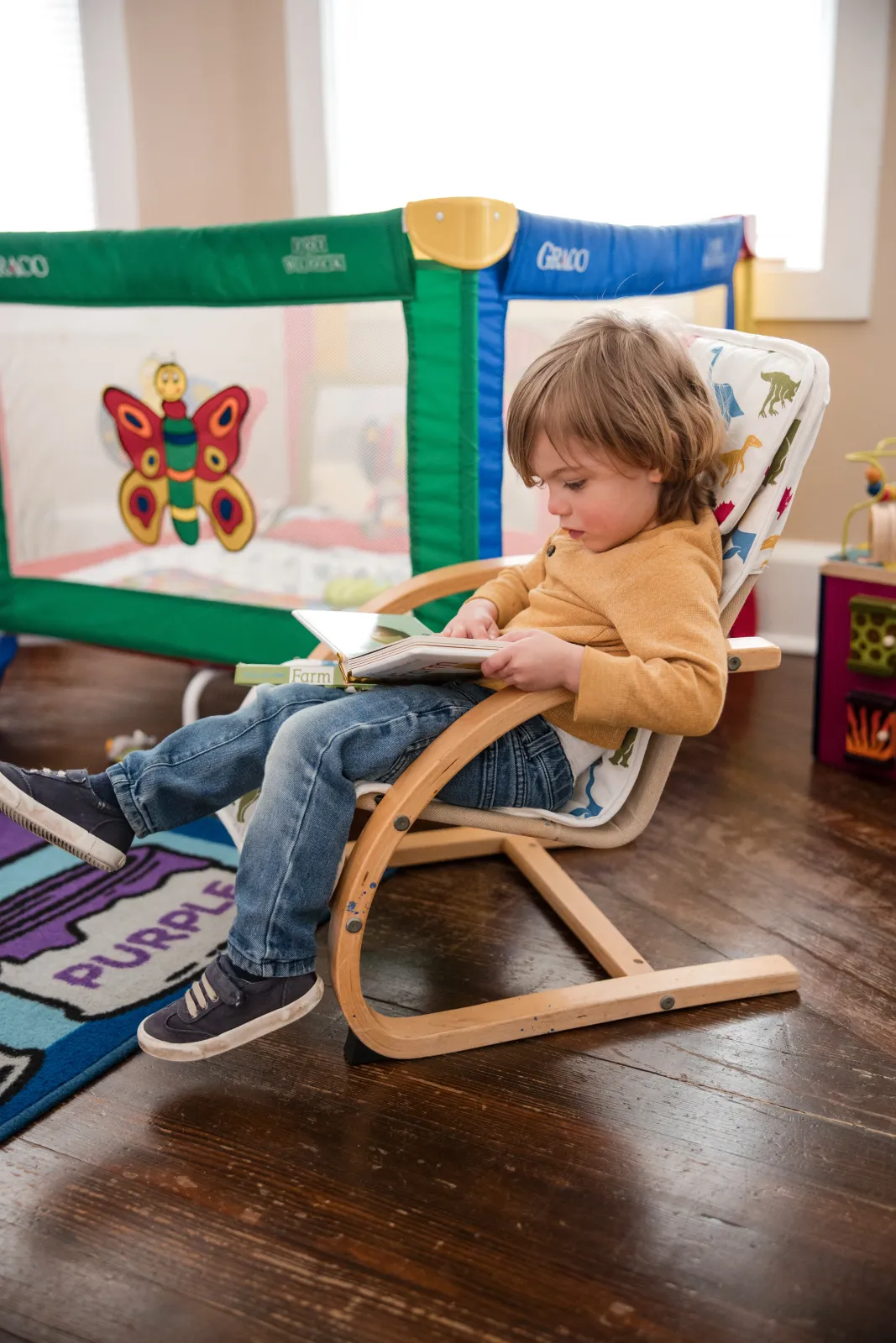 A child relaxing in a wooden rocker, looking through a picture book.